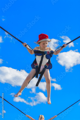 Children jumping on a trampoline with rubber ropes against the blue sky. Adventure and extreme sports. The concept of summer recreation, jumping.