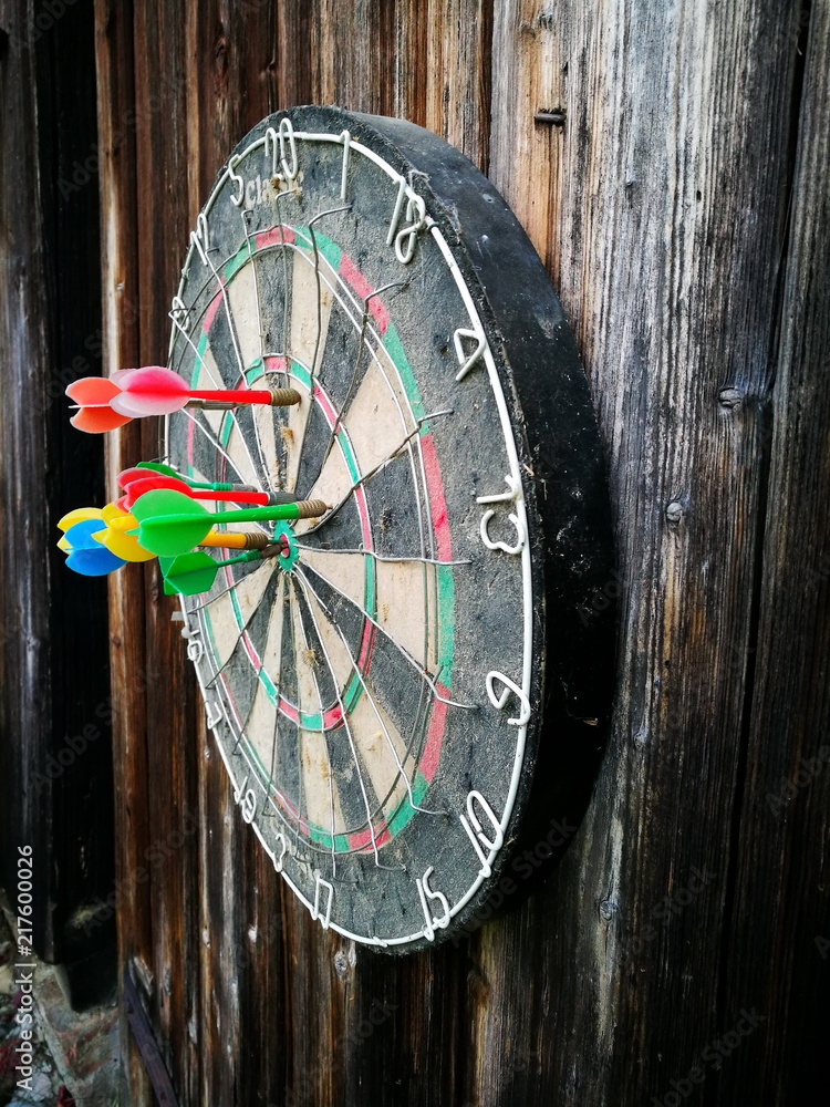 Alte Dartscheibe mit bunten Dartpfeilen aus Plastik auf dem dunklen Holz  einer Scheunentür in Rudersau bei Rottenbuch im schönen Oberbayern –  Stock-Foto | Adobe Stock