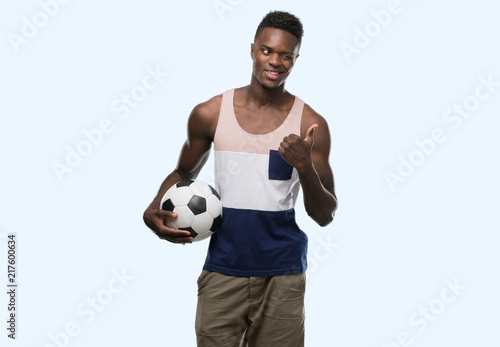 Young african american man holding soccer football ball pointing with hand and finger up with happy face smiling