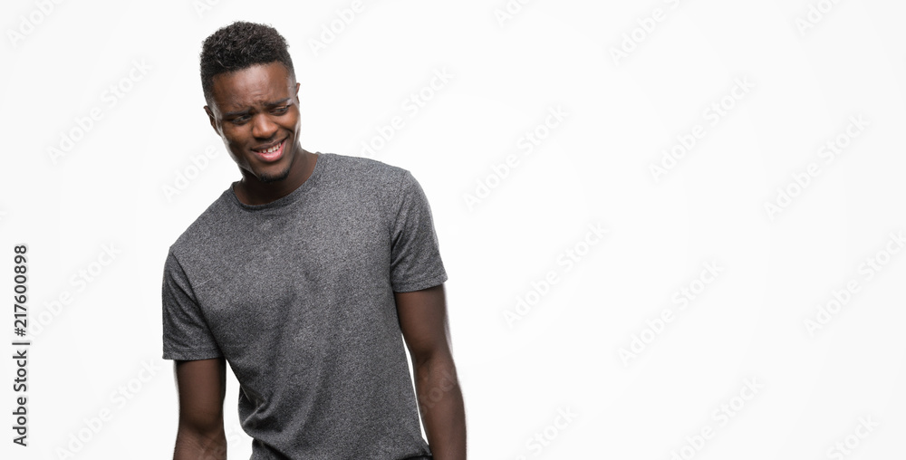 Young african american man wearing grey t-shirt looking away to side with smile on face, natural expression. Laughing confident. Young african american man wearing grey t-shirt looking away to side with smile on face, natural expression. Laughing confident.