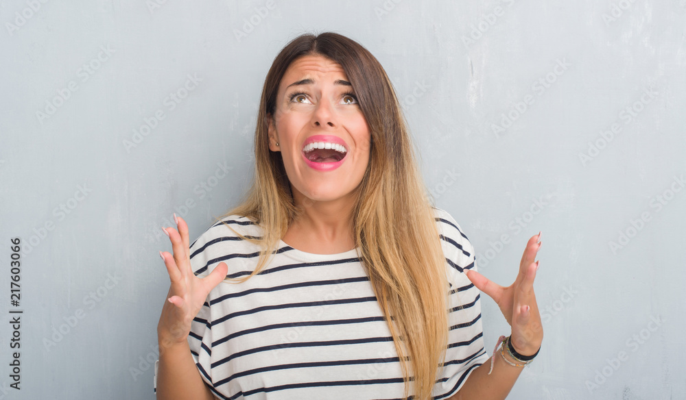 Young adult woman over grunge grey wall wearing navy t-shirt crazy and mad shouting and yelling with aggressive expression and arms raised. Frustration concept. Young adult woman over grunge grey wall wearing navy t-shirt crazy and mad shouting and yelling with aggressive expression and arms raised. Frustration concept.