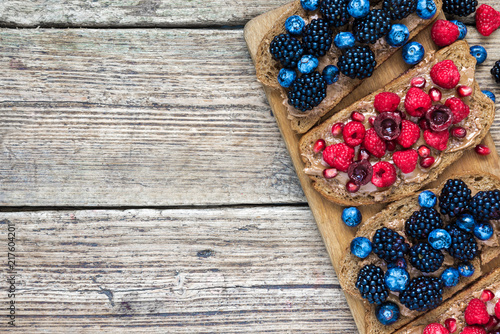whole grain bread toasts with peanut butter, fresh berries and pomegranate seeds on rustic wooden table