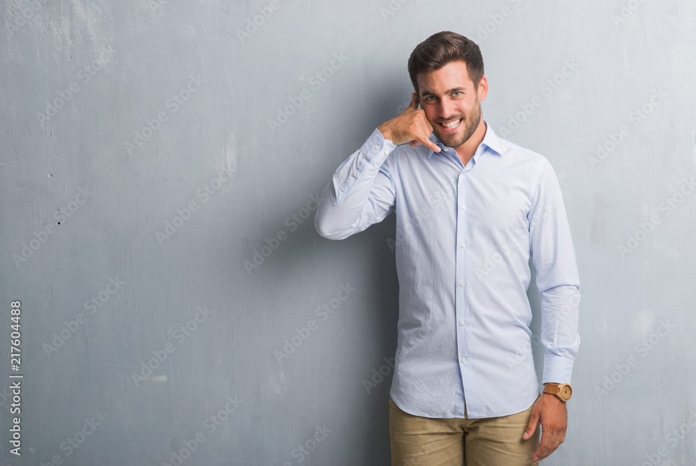 Handsome young business man over grey grunge wall wearing elegant shirt smiling doing phone gesture with hand and fingers like talking on the telephone. Communicating concepts.
