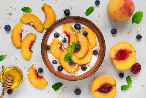Fototapeta Naklejka Na Ścianę i Meble -  yogurt with peaches, oats, blueberries, honey and mint in a bowl for healthy breakfast on white marble background
