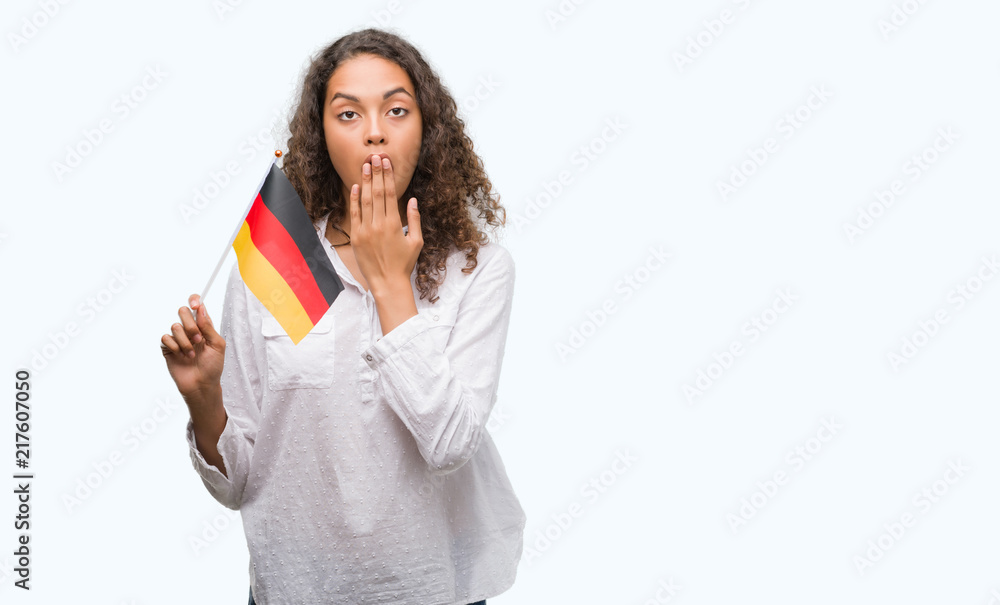 Young hispanic woman holding flag of Germany cover mouth with hand shocked with shame for mistake, expression of fear, scared in silence, secret concept Young hispanic woman holding flag of Germany cover mouth with hand shocked with shame for mistake, expression of fear, scared in silence, secret concept