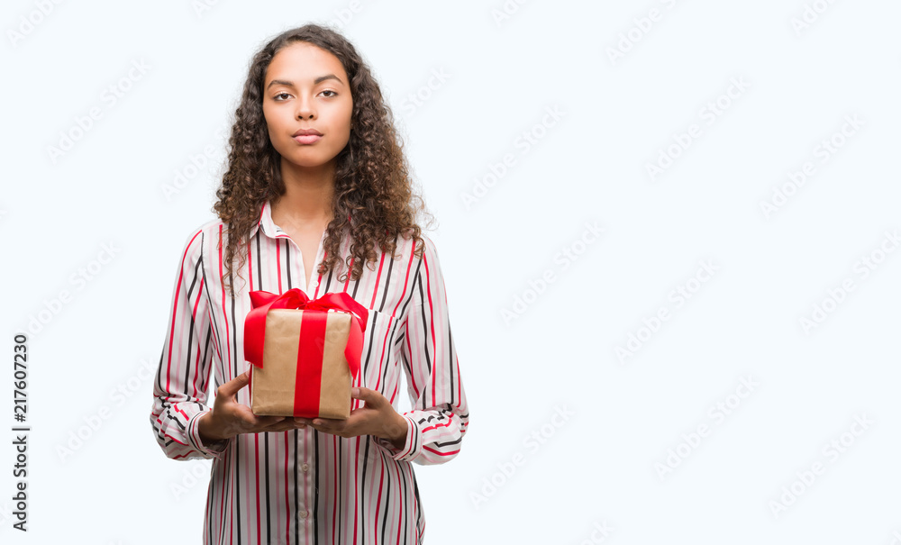 Young hispanic woman in love holding present with a confident expression on smart face thinking serious Young hispanic woman in love holding present with a confident expression on smart face thinking serious