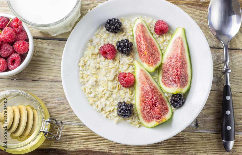 Bowl of oatmeal porridge with figs, raspberries and blackberries on teal rustic table Bowl of oatmeal porridge with figs, raspberries and blackberries on teal rustic table