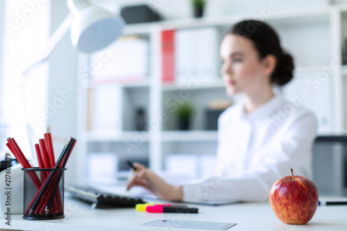 Young girl in the office with an apple. A photograph with a depth of field, a highlighted focus on an apple. photo