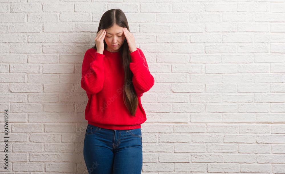 Young Chinese woman over brick wall with hand on head for pain in head because stress. Suffering migraine. Young Chinese woman over brick wall with hand on head for pain in head because stress. Suffering migraine.