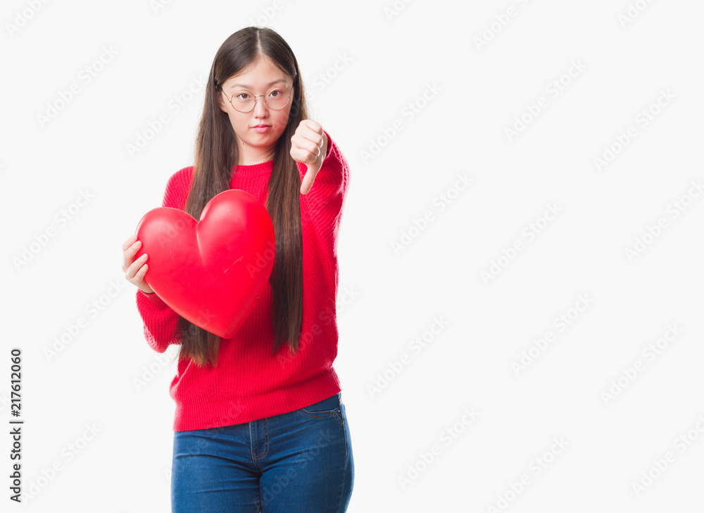 Young Chinese woman wearing graduate uniform red heart with angry face, negative sign showing dislike with thumbs down, rejection concept Young Chinese woman wearing graduate uniform red heart with angry face, negative sign showing dislike with thumbs down, rejection concept