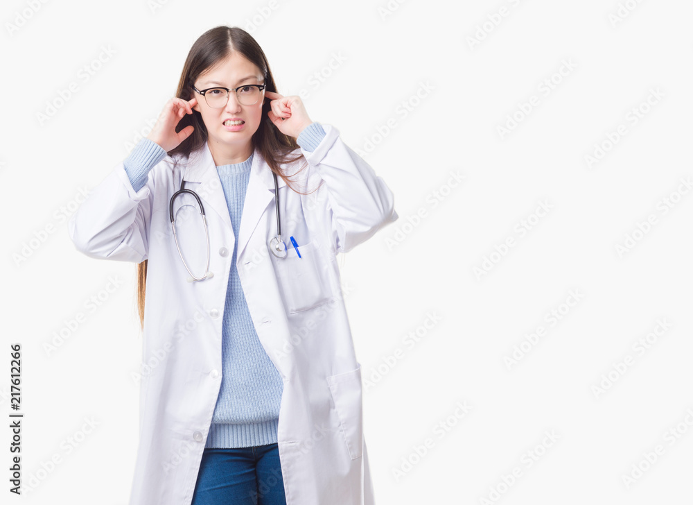 Young Chinese doctor woman over isolated background covering ears with fingers with annoyed expression for the noise of loud music. Deaf concept. Young Chinese doctor woman over isolated background covering ears with fingers with annoyed expression for the noise of loud music. Deaf concept.