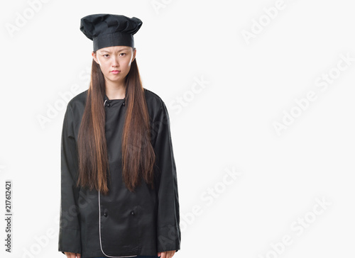 Young Chinese woman over isolated background wearing chef uniform skeptic and nervous, frowning upset because of problem. Negative person.