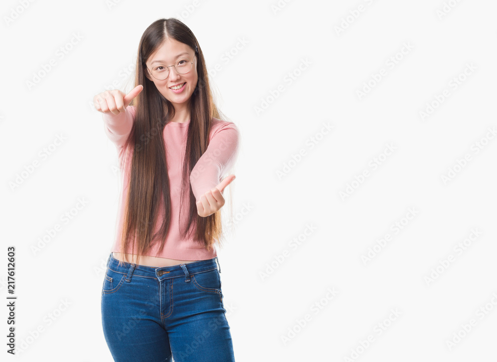 Young Chinese woman over isolated background wearing glasses approving doing positive gesture with hand, thumbs up smiling and happy for success. Looking at the camera, winner gesture. Young Chinese woman over isolated background wearing glasses approving doing positive gesture with hand, thumbs up smiling and happy for success. Looking at the camera, winner gesture.