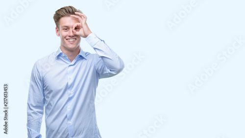 Young handsome blond man with happy face smiling doing ok sign with hand on eye looking through fingers © Krakenimages.com