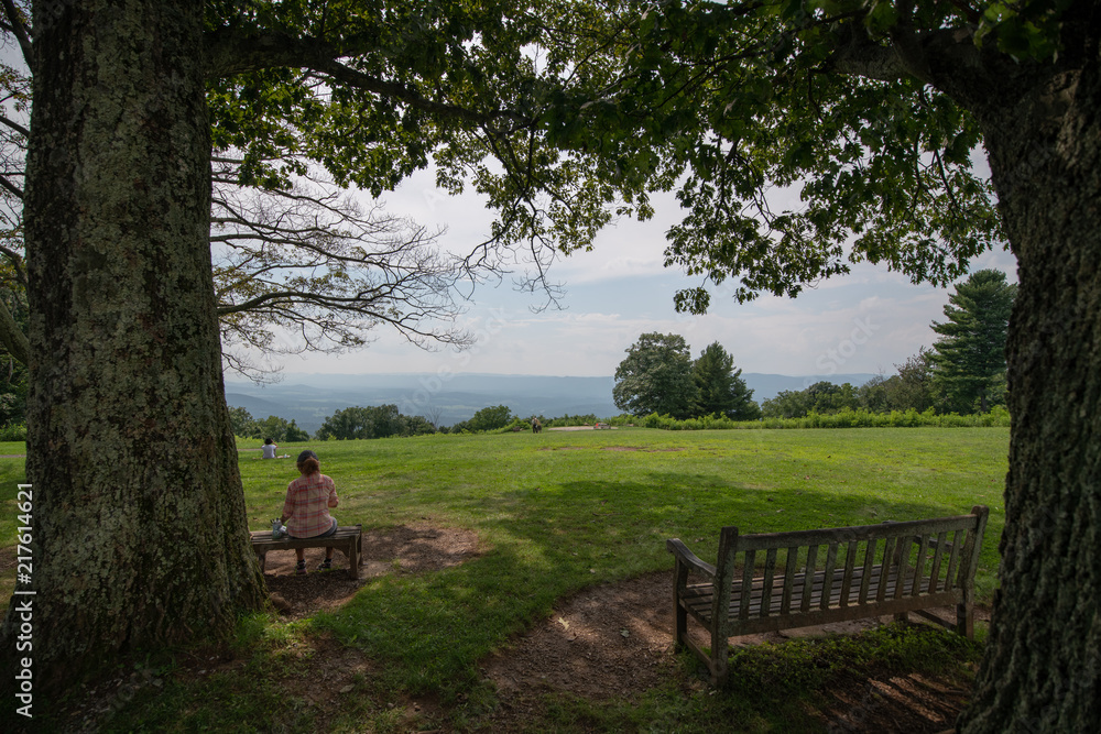 A woman sits on a blanket beneath a tree relaxing in the summer sun as she enjoys the view of the Appalachian Mountains from Shenandoah National Park and Skyline Drive
