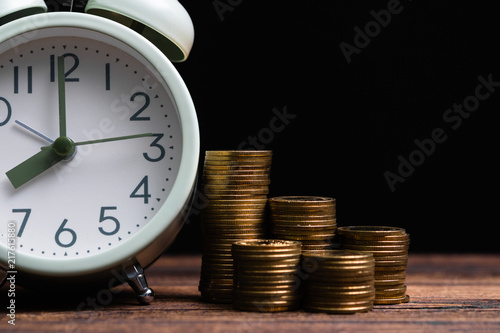 Alarm clock and coins stacks on working table in dark room, time for savings money concept, banking and business concept.