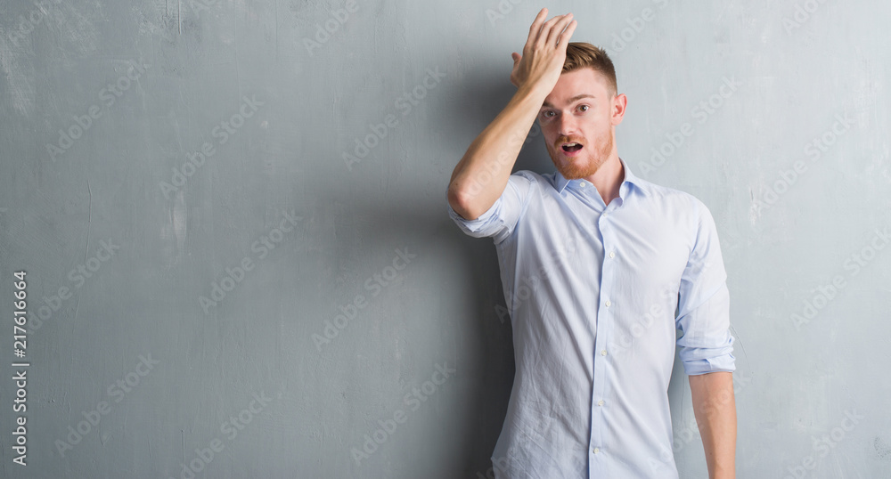 Young redhead business man over grey grunge wall surprised with hand on head for mistake, remember error. Forgot, bad memory concept. Young redhead business man over grey grunge wall surprised with hand on head for mistake, remember error. Forgot, bad memory concept.