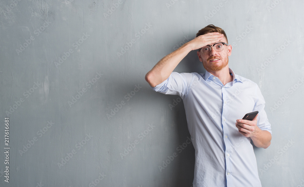 Young redhead man over grey grunge wall sending message using smartphone stressed with hand on head, shocked with shame and surprise face, angry and frustrated. Fear and upset for mistake. Young redhead man over grey grunge wall sending message using smartphone stressed with hand on head, shocked with shame and surprise face, angry and frustrated. Fear and upset for mistake.