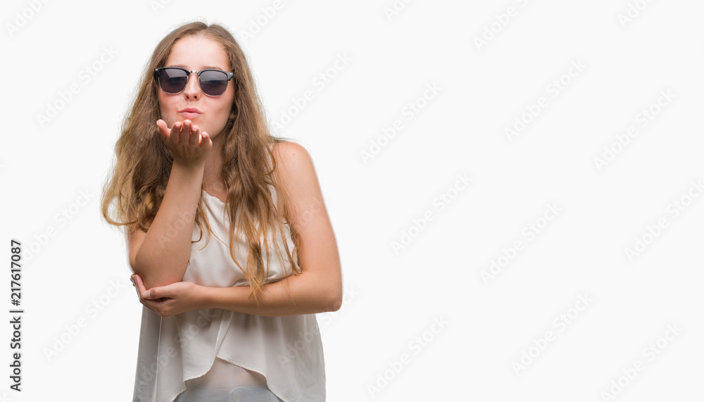 Young blonde woman wearing sunglasses looking at the camera blowing a kiss with hand on air being lovely and sexy. Love expression. Young blonde woman wearing sunglasses looking at the camera blowing a kiss with hand on air being lovely and sexy. Love expression.
