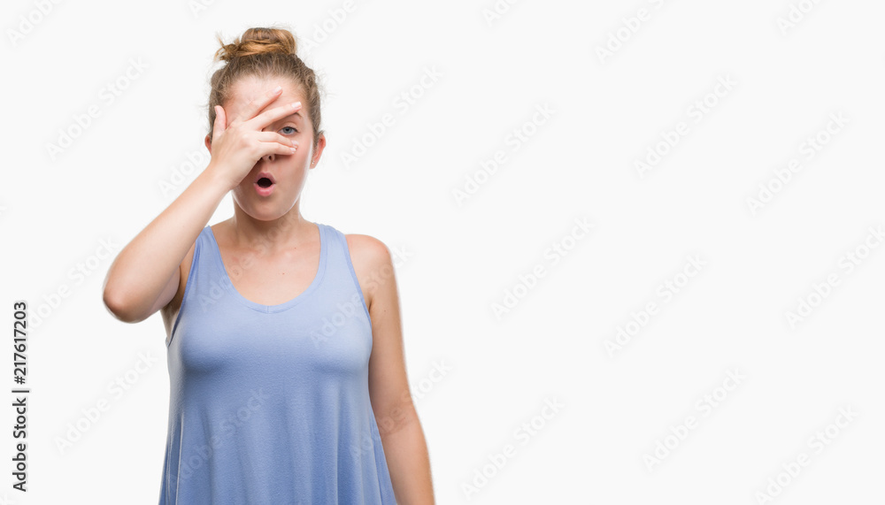 Young blonde woman peeking in shock covering face and eyes with hand, looking through fingers with embarrassed expression. Young blonde woman peeking in shock covering face and eyes with hand, looking through fingers with embarrassed expression.