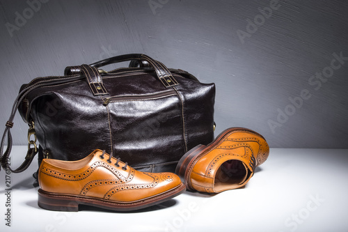 Pair of Luxury Male Tanned Full Broggued Oxford Calf Leather Shoes Along With Dakr Brown Leather Travel Bag on White Surface. photo