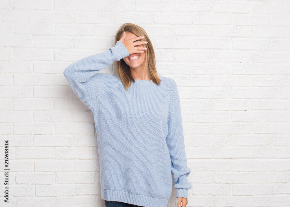 Beautiful young woman over white brick wall smiling and laughing with hand on face covering eyes for surprise. Blind concept. Beautiful young woman over white brick wall smiling and laughing with hand on face covering eyes for surprise. Blind concept.