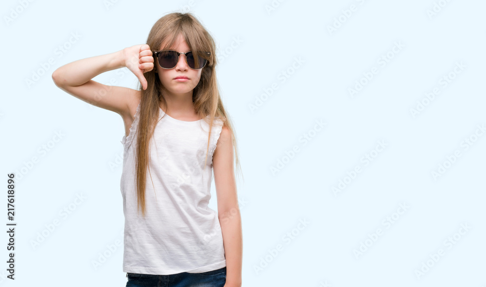 Fototapeta premium Young blonde toddler wearing sunglasses with angry face, negative sign showing dislike with thumbs down, rejection concept