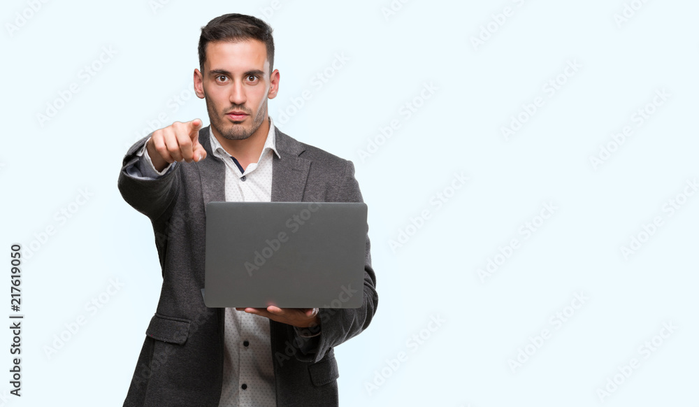 Handsome young man using computer laptop pointing with finger to the camera and to you, hand sign, positive and confident gesture from the front Handsome young man using computer laptop pointing with finger to the camera and to you, hand sign, positive and confident gesture from the front