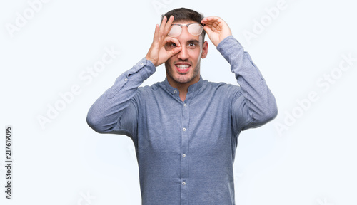 Wallpaper Mural Handsome young elegant man wearing glasses doing ok gesture with hand smiling, eye looking through fingers with happy face. Torontodigital.ca