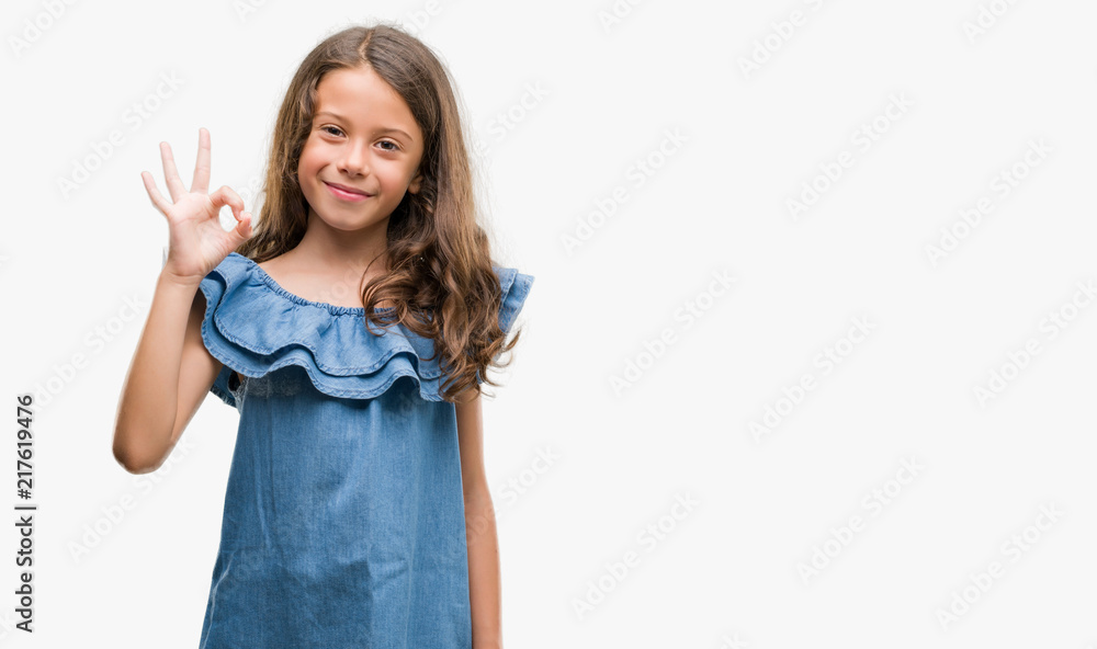 Brunette hispanic girl wearing denim dress doing ok sign with fingers, excellent symbol Brunette hispanic girl wearing denim dress doing ok sign with fingers, excellent symbol