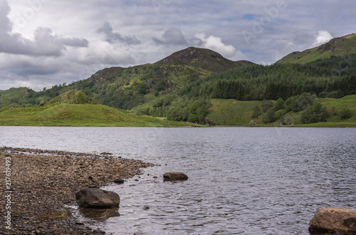 Bridge of Orchy, Scotland, UK - June 12, 2012: Bluesh loch of Tulla surrounded by green hills, some covered by forest, under a heavy cloudscape. Left side shows rocky beach. photo