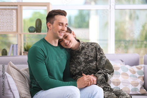 Woman in military uniform with her husband on sofa at home photo