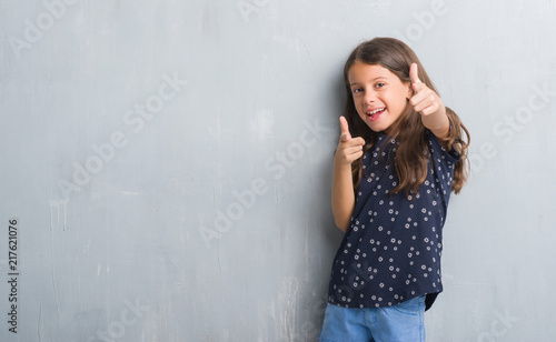 Young hispanic kid over grunge grey wall pointing fingers to camera with happy and funny face. Good energy and vibes.