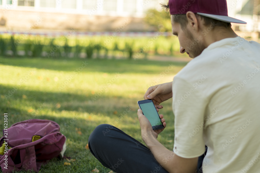 young hipster in casual holding mobile phone in the city park during summer day young hipster in casual holding mobile phone in the city park during summer day