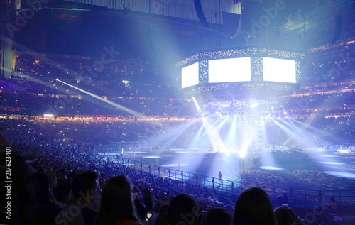 Concert stage with shining lights and crowd at a performance. Rock music event at a stadium with colorful spotlights and projectors.