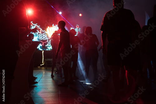 People dance at a nightclub at night in silhouette with different color lights and digital effects