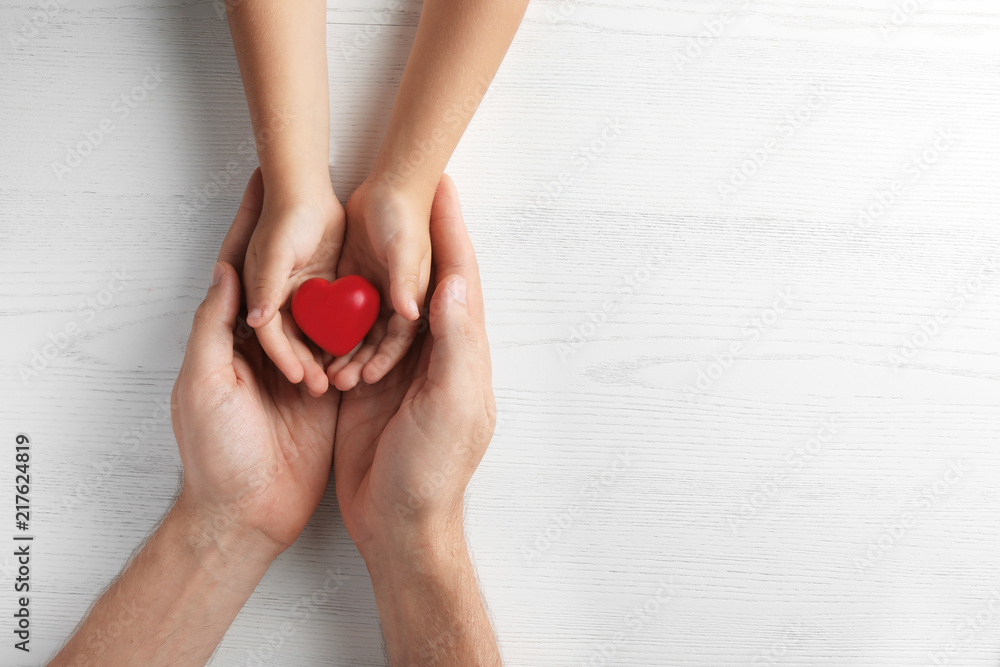 Family holding small red heart in hands on wooden background Family holding small red heart in hands on wooden background