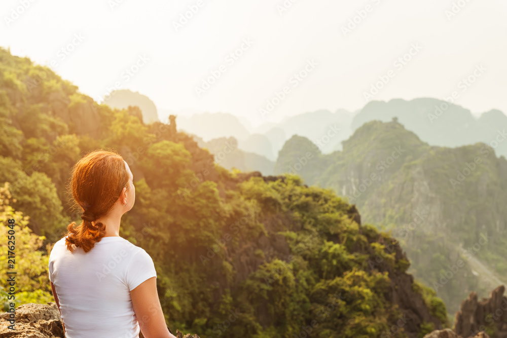 Naklejka premium back view woman tourist looking far away and enjoying valley and hills view from top of a mountain