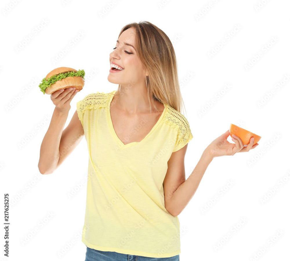 Young woman holding burger and grapefruit on white background. Choice between diet and unhealthy food Young woman holding burger and grapefruit on white background. Choice between diet and unhealthy food