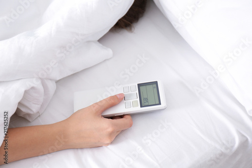 Woman holding air conditioner remote control in bed, focus on hand