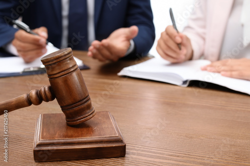 Wooden gavel and blurred lawyer with client on background