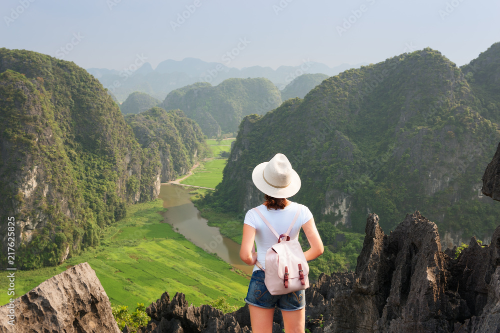 Young tourist with backpack enjoying valley view from top of a mountain