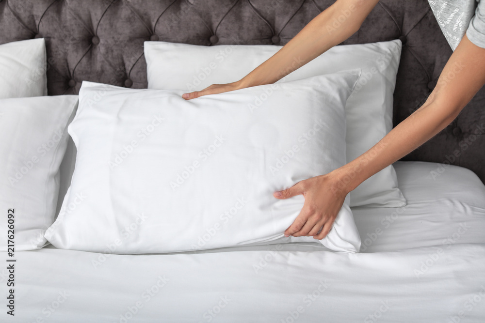 Young woman plumping white pillow on bed, closeup Young woman plumping white pillow on bed, closeup