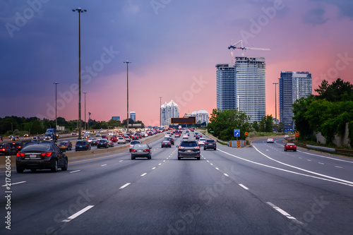 Night traffic. Cars on highway road at sunset evening in typical busy american city. Beautiful amazing night urban view with red, yellow and blue sky clouds. Sundown in downtown. © anoushkatoronto