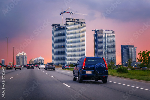 Night traffic. Cars on highway road at sunset evening in typical busy american city. Beautiful amazing night urban view with red, yellow and blue sky clouds. Sundown in downtown.