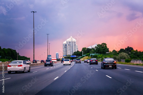 Night traffic. Cars on highway road at sunset evening in typical busy american city. Beautiful amazing night urban view with red, yellow and blue sky clouds. Sundown in downtown. © anoushkatoronto