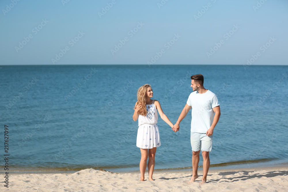 Happy young couple holding hands at beach on sunny day Happy young couple holding hands at beach on sunny day