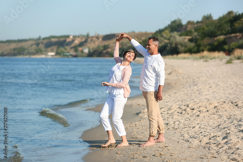 Happy mature couple dancing at beach on sunny day