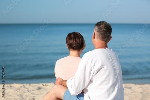 Happy mature couple sitting together at beach on sunny day