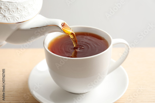 Pouring hot tea into porcelain cup on wooden table